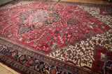 Mehrivan carpet's corner with cherry red field of geometric blossoms and navy border.