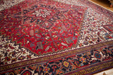 Angled view of the vintage Mehrivan carpet's red medallion and navy samovar border.