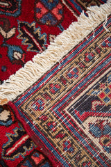 A folded corner of a vintage Mehrivan rug showing the hand-knotted weave, geometric border, and ivory fringe.
