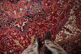 A person's perspective on the plush, densely patterned wool pile of a vintage Heriz carpet.