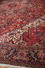 Angled view of a vintage Heriz carpet showing the fine weave, serrated leaf border, and rich ruby red field.