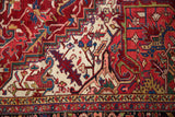 Intricately drawn serrated leaves in gem-tones on the ivory corner of a vintage Heriz carpet.