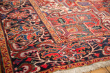 Heriz carpet navy border close-up: sprawling floral elements in black cherry red, sapphire, and gold.