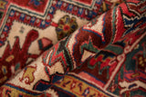 Rolled vintage Heriz carpet pile showing navy blue, black cherry red, and ivory patterns.