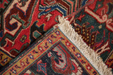 Vintage Heriz rug corner showing red floral field, geometric navy border, and ivory fringe.