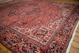 Vintage Heriz rug corner featuring geometric vinery and floral motifs in brick red, navy, and ivory.