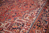 Vintage Heriz carpet with elaborate geometric vinery and floral design, pale brick red, navy blue, and visible side selvage.