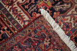 Vintage Heriz rug corner: navy, brick red geometric floral pattern, red selvage, white fringe.