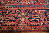 Close-up of hand-knotted Heriz carpet border with geometric vinery in navy, brick red, gold.