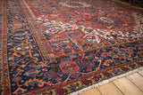 Vintage Heriz carpet corner with navy border, brick red field, and ivory fringe.