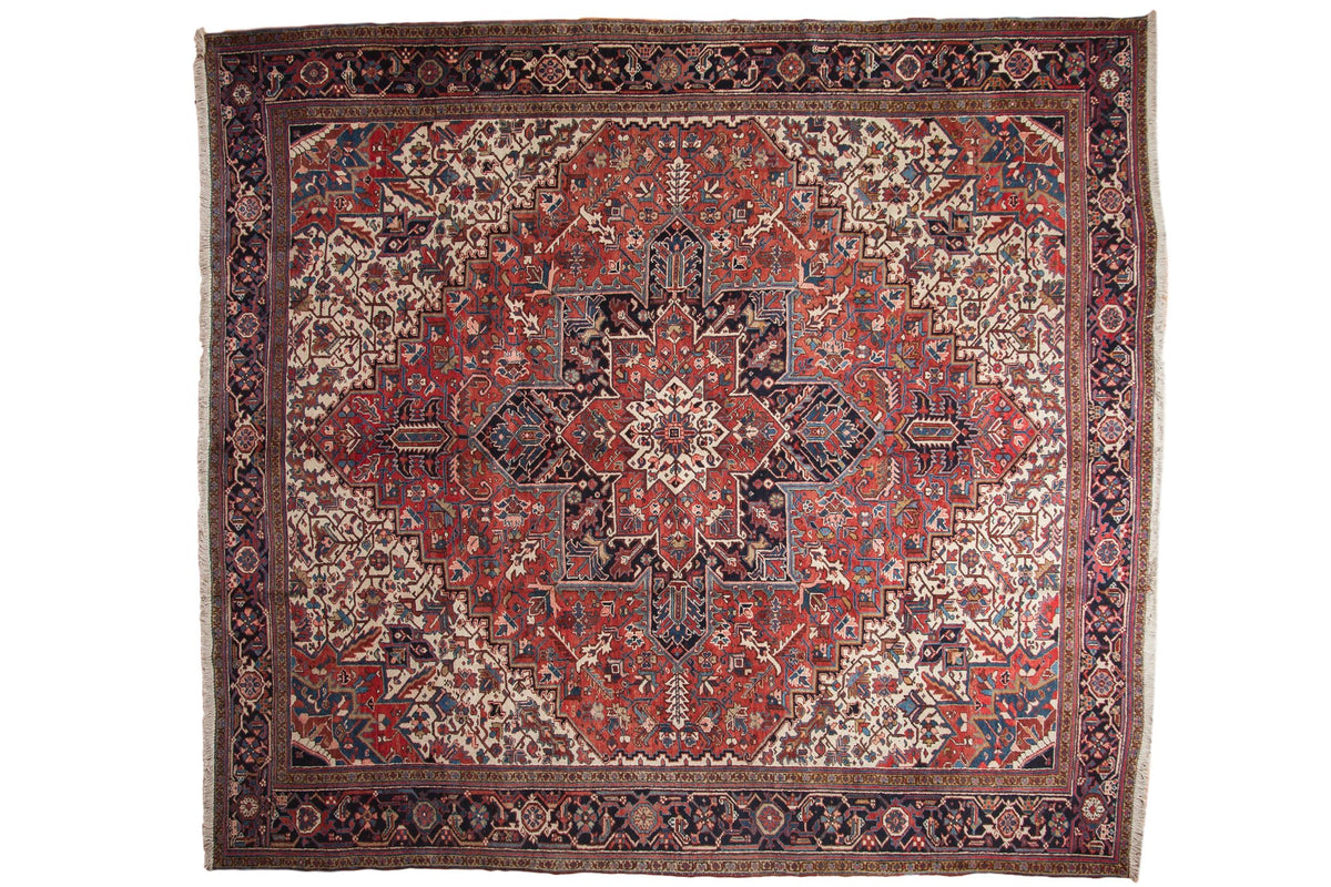 Oversize vintage Heriz square carpet with a bold geometric medallion in brick red, navy blue, and ivory.