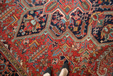 Angled view of the full pile and geometric patterns on a vintage Mehrivan carpet in rust red and navy blue.