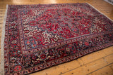 Diagonal view of a vintage Mehrivan carpet's red field and dark navy turtle design border.