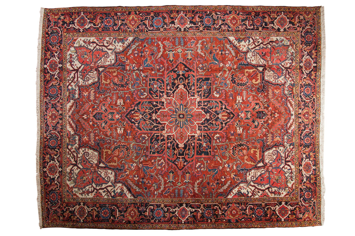 Vintage Persian Heriz carpet with a large geometric medallion on a brick red field with navy blue and ivory details.