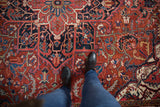 Detailed overhead view of a vintage Heriz carpet's full pile and intricate red and navy pattern.