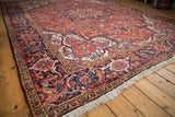 A vintage Heriz rug's corner with a detailed navy Samovar Turtle border and rich brick-red pile.