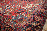 A vintage Heriz carpet's detailed navy floral border next to its geometric red field and plush wool pile.