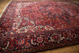 Angled view of a vintage Heriz rug's navy blue border with floral motifs next to its dense, cherry red field.