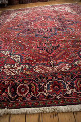 Plush, full pile of a vintage Persian Heriz carpet, with a detailed navy blue and cherry red border in the foreground.
