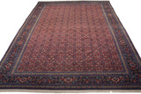 Vintage Persian Tabriz carpet viewed from an angle, showing the dense red Herati field and complex blue border.