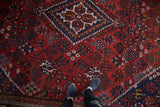 Feet on hand-knotted vintage Joshegan carpet, navy diamond medallion, rust floral motifs.