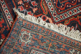 Vintage Joshegan carpet corner, revealing hand-knotted back weave, rustic red, navy patterns, and fringe.