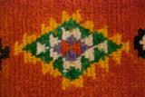 Serrated diamond medallion with emerald green and saffron yellow on a plush, rust-orange wool pile.