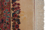 Minor imperfection on the ivory field of a vintage Kerman rug, next to its floral border and fringe.