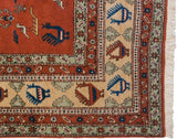 Corner of vintage Meshkin carpet: terracotta field with playful bird motifs, geometric borders, and white fringe.