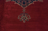 Elongated finial motif with navy and silver details on the vintage Oushak's red wool pile.