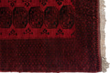 Corner of a vintage Ersari carpet showing black gul motifs, a complex border, and original fringe.