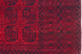 Detail of a vintage Afghani carpet with cherry red gul motifs beside intricate navy geometric borders.