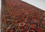 A long perspective on a vintage Persian runner showing its red Herati field and geometric border.