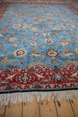 Angled view of a vintage Qom carpet's corner, showing the pictorial red border and intricate animal designs.