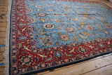 Angled view of a vintage Qom carpet showing its red animal border and intricate blue floral field.