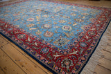 Angled view of a vintage Qom carpet showing the intricate sky blue field and pictorial red border.