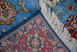 The corner of a hand-knotted Persian rug with its original selvage, white fringe, and dense floral pile.