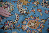 A hand rests on the pictorial tiger motif of a vintage Persian Qom rug with a sky blue pile.