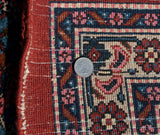 A coin for scale highlights the dense hand-knotted pile and intact rust selvage of this Persian rug.