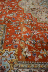 Burnt orange Tabriz rug close-up showing ornate floral vinery with soft patina.