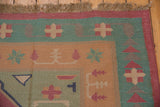 Dhurrie rug corner: geometric motifs, dusty seafoam, pale copper, raspberry red, with fringe.
