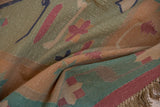 Textured fold of vintage Dhurrie rug with pale raspberry, dusty seafoam motifs, and fringe.