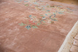 Plush dusty rose pile showing pastel floral vines and ivory fringe on an Art Deco carpet.