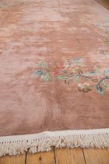 Close-up of a vintage carpet's plush dusty rose pile, Art Deco foliage, and ivory knotted fringe.