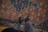 Feet on a vintage Ardebil carpet, showing terra cotta rust and sky blue Herati pattern.