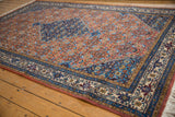 Terra cotta field with repeating Herati motif, sapphire blue spandrel, and intricate beige border.