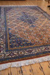 Ardebil rug's burnt orange field with Herati motif, detailed blue border, and ivory fringe.