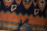Feet on vintage Meshkin rug, showcasing navy blue field, finned motifs, and intricate geometric border.