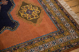 Finned contour medallion on dusty sandalwood field, framed by navy and gold geometric borders.