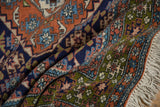 Folded vintage Ardebil rug pile with Herati floral motifs, rich navy, terra cotta, green, and fringe.